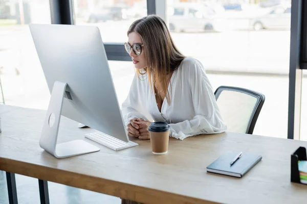 Jovem empresária em óculos olhando para monitor de computador no escritório — Fotografia de Stock