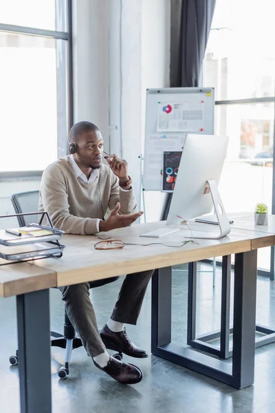 Opérateur afro-américain tenant le microphone tout en parlant au bureau — Photo de stock