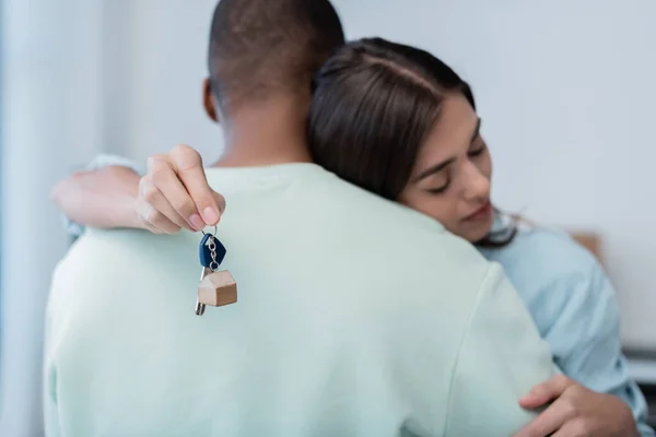 Mujer joven sosteniendo la llave de nuevo apartamento y abrazando novio afroamericano - foto de stock