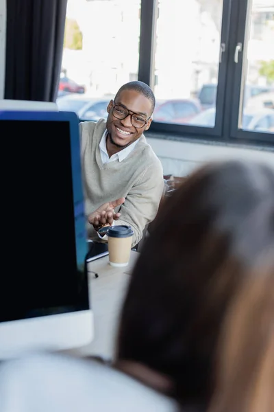 Щасливий афроамериканський чоловік в окулярах, вказуючи на розмиту жінку в офісі — стокове фото