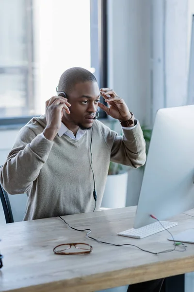 Afrikanisch-amerikanischer Bediener im Headset schaut auf Computermonitor — Stockfoto