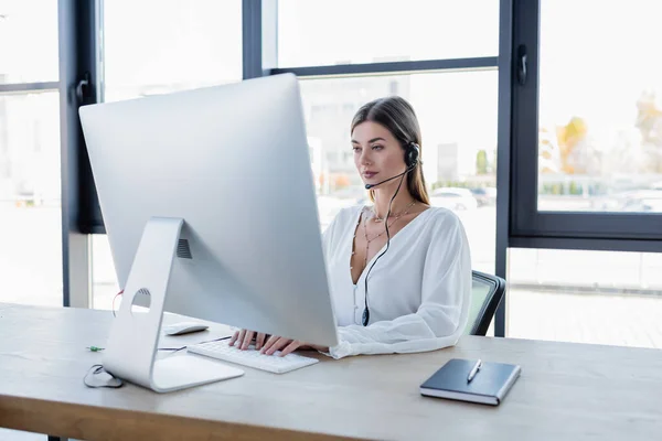 Pretty operator in headset using computer keyboard in office — Stock Photo