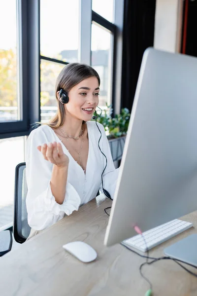 Cheerful operator in headset talking and using computer in office — Stock Photo