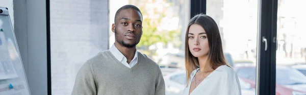 Hombre de negocios interracial y mujer de negocios mirando a la cámara en la oficina, pancarta - foto de stock