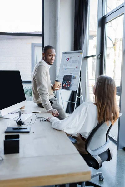 Hombre de negocios afroamericano sosteniendo taza de papel y hablando con su colega - foto de stock