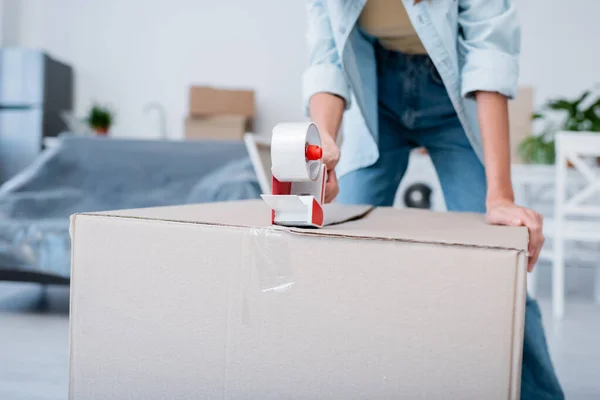 Cropped view of woman holding adjusting tape near carton box — Stock Photo