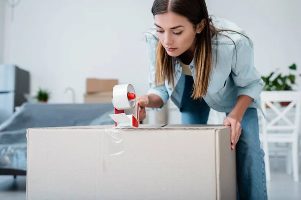 Jovem mulher segurando fita de ajuste perto da caixa de papelão — Fotografia de Stock