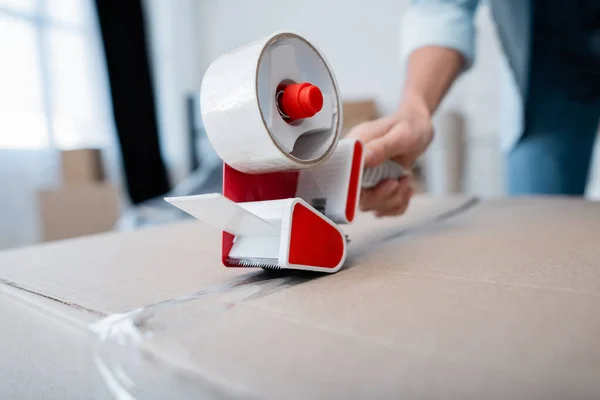 Partial view of woman holding adjusting tape while packing carton box — Stock Photo