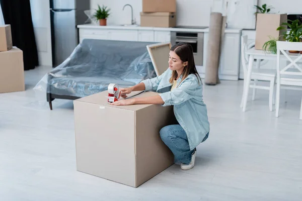 Молодая женщина держит регулирующую ленту и упаковку коробки в гостиной — стоковое фото
