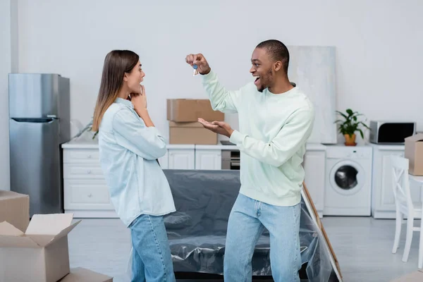 Happy african american man holding key near excited girlfriend in new apartment — Stock Photo