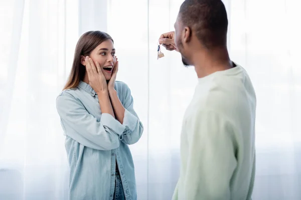 Desenfocado africano americano hombre sosteniendo llave cerca excitado novia en nuevo apartamento - foto de stock