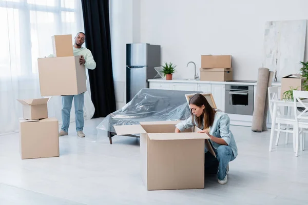 Young woman and african american man around boxes in new apartment — Stock Photo