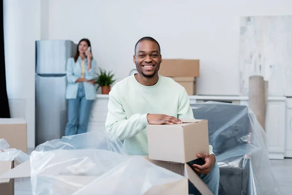 Glücklich afrikanisch-amerikanischer Mann auspackt Schachtel in der Nähe verschwommene Freundin — Stockfoto