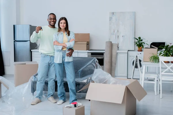 Glücklich afrikanisch-amerikanischer Mann hält Schlüssel, während er lächelnde Freundin in neuer Wohnung umarmt — Stockfoto