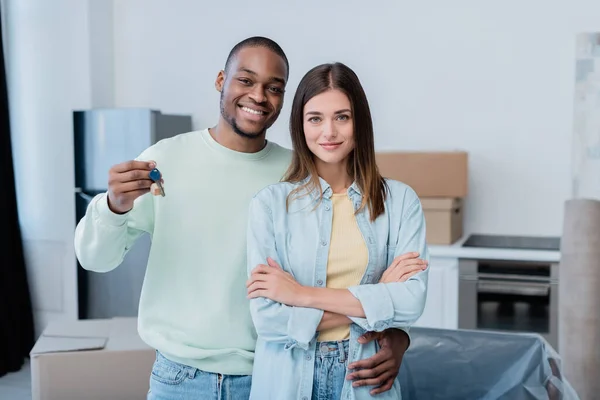 Happy african american man holding key while hugging pleased girlfriend in new apartment — Stock Photo