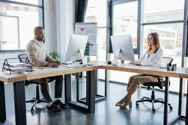 Kollegen mit Brille blicken im modernen Büro auf Computermonitore — Stockfoto