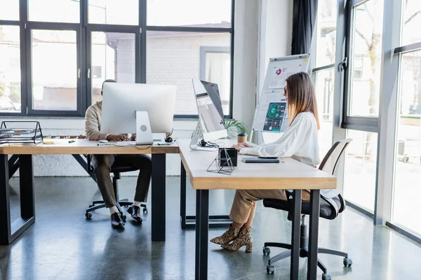 Geschäftsfrau mit Brille blickt auf Computerbildschirm, während sie mit einem Afroamerikaner in einem modernen Büro arbeitet — Stockfoto