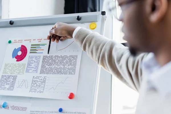 Verschwommener afrikanisch-amerikanischer Mann zeigt Infografik mit Stift auf Flipchart — Stockfoto