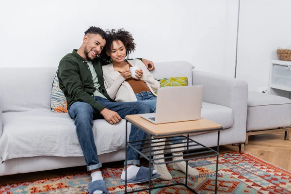 Alegre africano americano marido y embarazada esposa viendo película en portátil - foto de stock