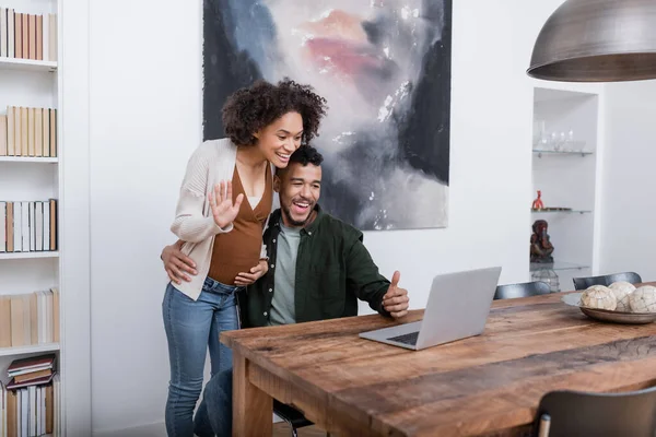 Glücklich schwangere afrikanisch-amerikanische Frau winkt Laptop nahe Ehemann zeigt Daumen nach oben — Stockfoto