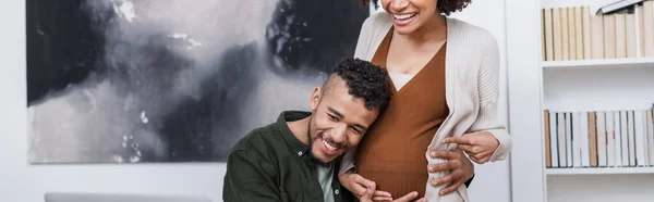 Gai enceinte afro-américaine femme pointant vers le ventre près mari heureux, bannière — Photo de stock