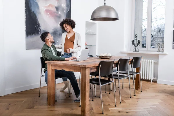 Glücklich schwangere afrikanisch-amerikanische Frau sieht Ehemann, der von zu Hause aus arbeitet — Stockfoto