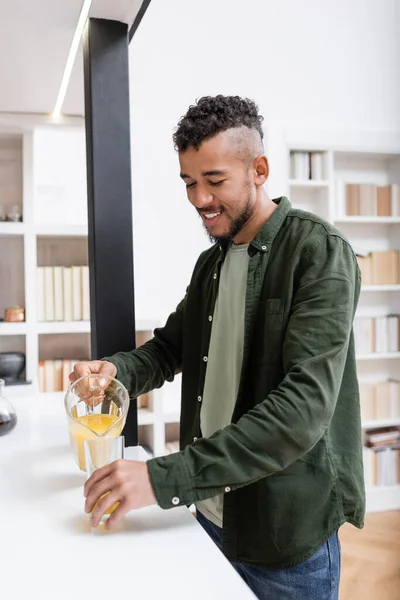 Pleased african american man pouring orange juice in glass — Stock Photo