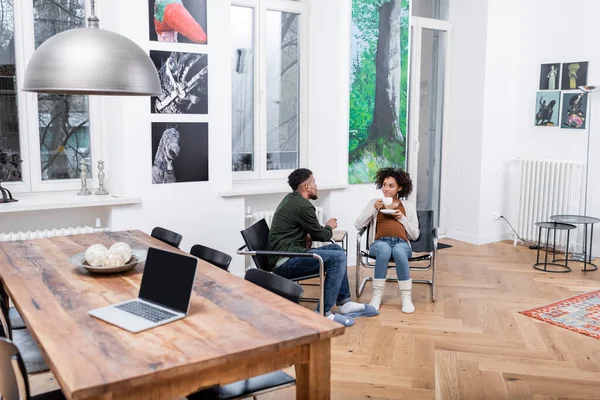 African american man looking at curly pregnant wife holding cup of tea — Stock Photo