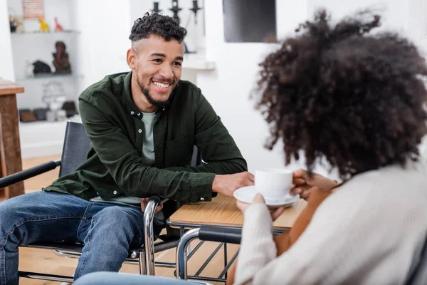 Fröhlicher afrikanisch-amerikanischer Mann blickt verschwommene schwangere Frau mit Tasse Tee an — Stockfoto