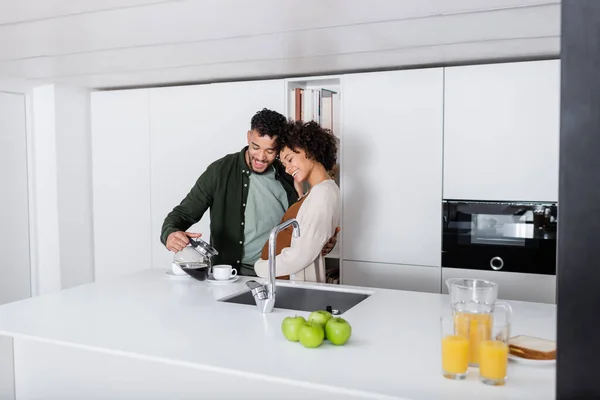 Feliz homem americano africano derramando café perto da esposa grávida na cozinha — Fotografia de Stock