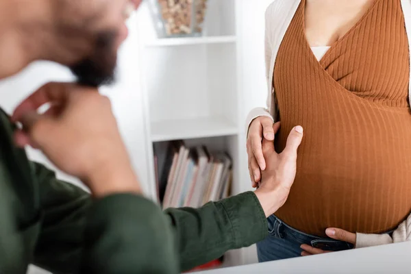 Abgeschnittene Ansicht eines verschwommenen afrikanisch-amerikanischen Mannes, der Bauch einer schwangeren Frau berührt — Stockfoto