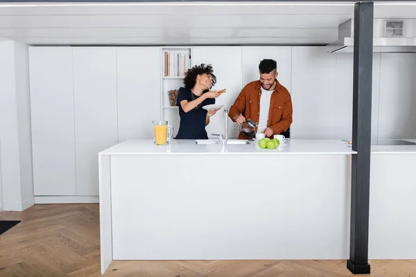 Feliz africano americano celebración sándwich cerca novio verter café en taza - foto de stock