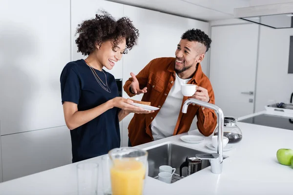 Glücklicher afrikanisch-amerikanischer Mann zeigt in Küche auf Sandwich neben Freundin — Stockfoto