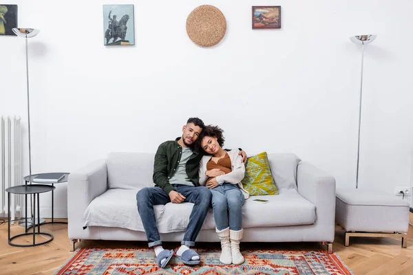 Feliz homem americano africano abraçando alegre esposa grávida na sala de estar moderna — Fotografia de Stock