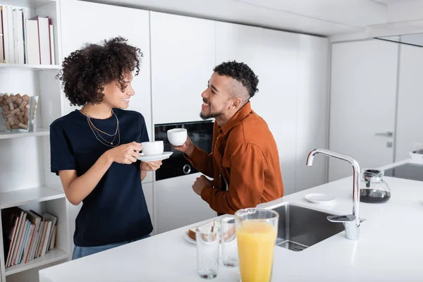 Feliz pareja afroamericana sosteniendo tazas de café en la cocina - foto de stock