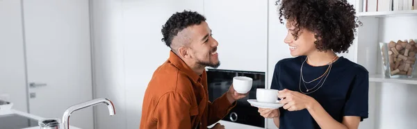 Feliz pareja afroamericana sosteniendo tazas de café en la cocina, pancarta - foto de stock