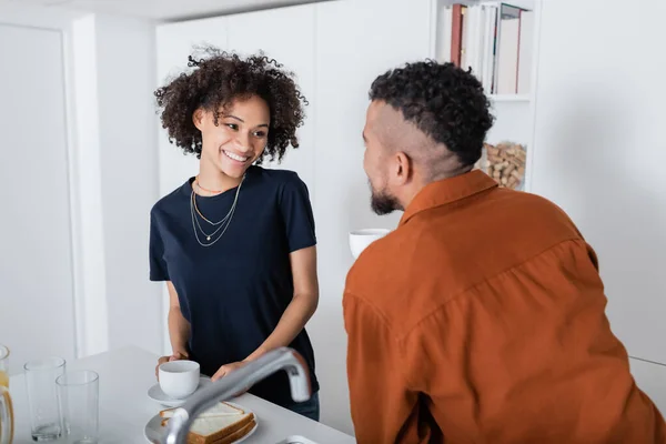 Fröhliche afrikanisch-amerikanische Frau schaut verschwommenen Freund in Küche an — Stockfoto