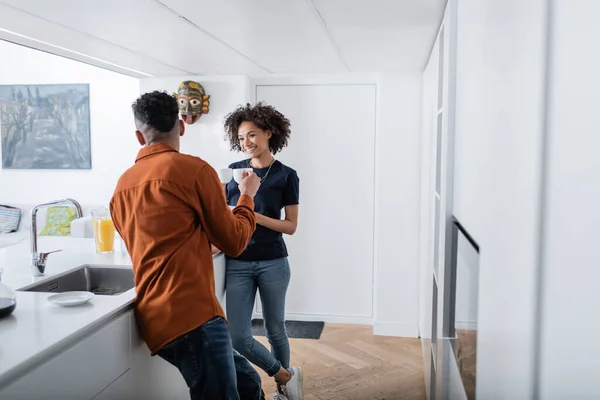 Cheerful african american couple holding cups of coffee in kitchen — Stock Photo