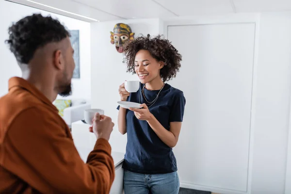 Allegra donna afro-americana guardando una tazza di caffè vicino al fidanzato offuscato — Foto stock