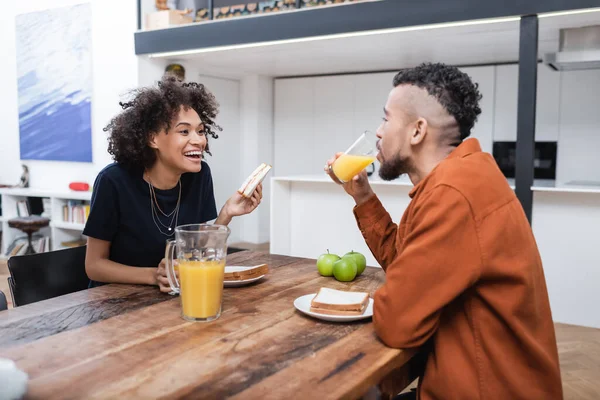 Fröhliche afrikanisch-amerikanische Frau hält Sandwich, während sie mit Freund zu Mittag isst — Stockfoto