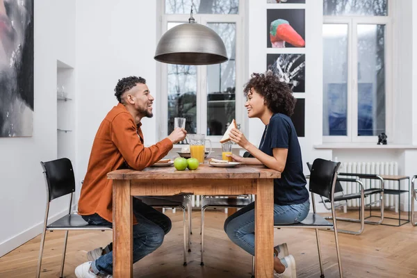 Happy african american woman holding sandwich and having lunch with cheerful boyfriend — Stock Photo