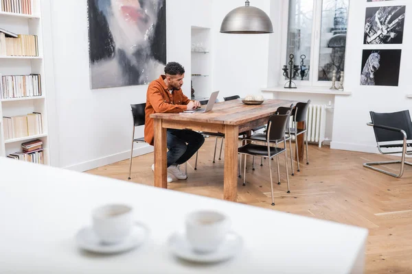 Freelancer afroamericano usando laptop mientras trabaja desde casa - foto de stock