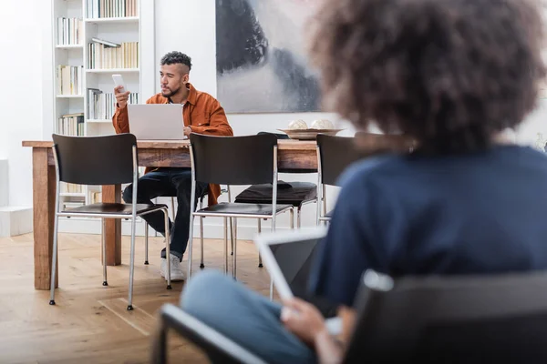 Afrikanisch-amerikanischer Freiberufler mit Smartphone, das von zu Hause aus in der Nähe der lockigen Freundin mit digitalem Tablet arbeitet — Stockfoto