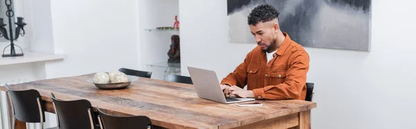 Афроамериканський фрілансер, який друкує на ноутбуці під час роботи з дому, банер — стокове фото