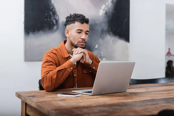 Freelancer afro-americano olhando para laptop enquanto trabalhava em casa — Fotografia de Stock