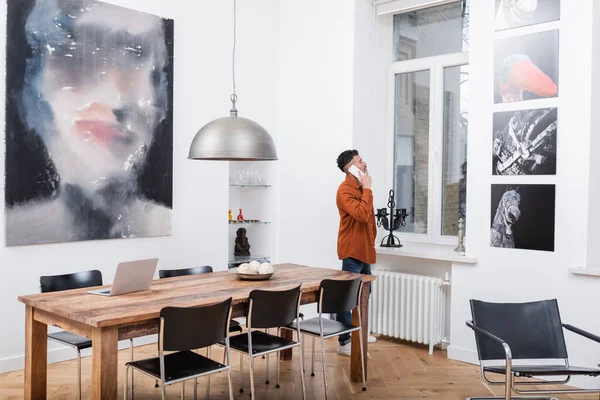 African american freelancer talking on smartphone and looking at window in modern apartment — Stock Photo