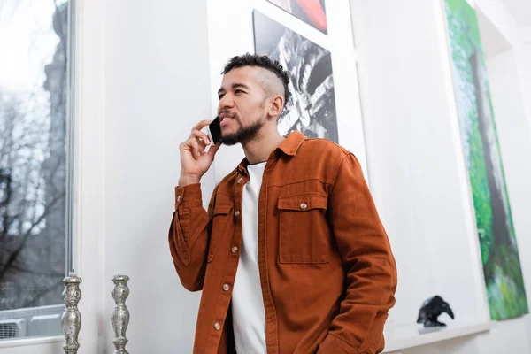 Encaracolado homem americano africano falando no smartphone no apartamento moderno — Fotografia de Stock