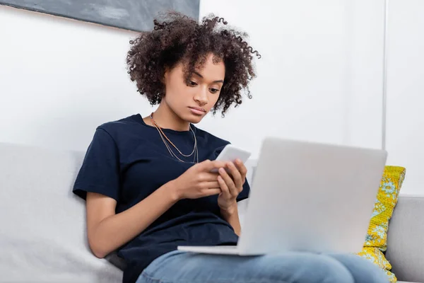 Lockige Afroamerikanerin benutzt Handy in der Nähe von Laptop — Stockfoto