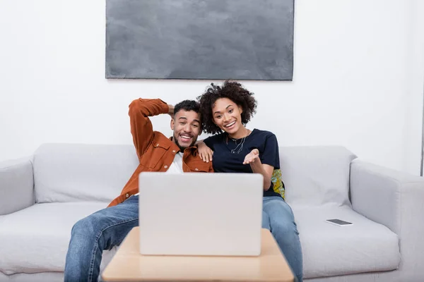 Happy young african american woman pointing with hand at laptop while watching movie with boyfriend — Stock Photo