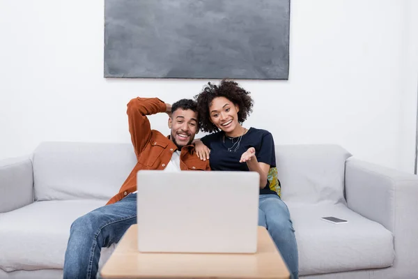 Glückliche junge afrikanisch-amerikanische Frau zeigt mit der Hand auf Laptop, während Film mit Freund — Stockfoto